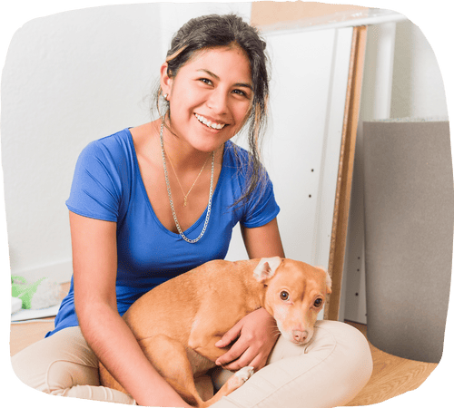 Young woman sitting on the floor smiling warmly while gently cuddling a tan dog in her lap