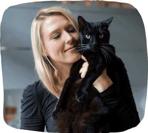 Smiling woman lovingly holds a sleek black cat indoors, showcasing the trust and comfort shared between pets and their dedicated sitters